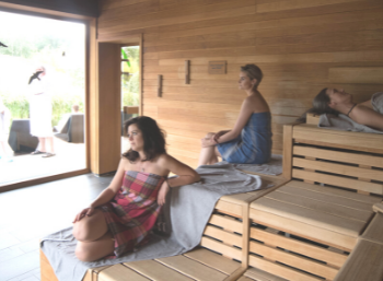 Mehrere Personen in einer Sauna mit Blick nach draußen auf weitere Personen.